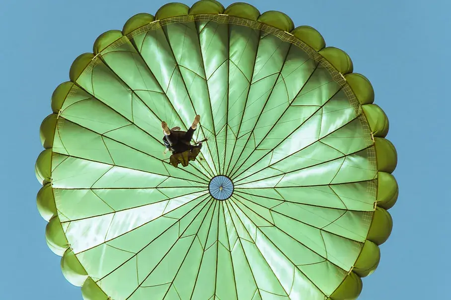 Skydiver under a green round parachute against a blue sky