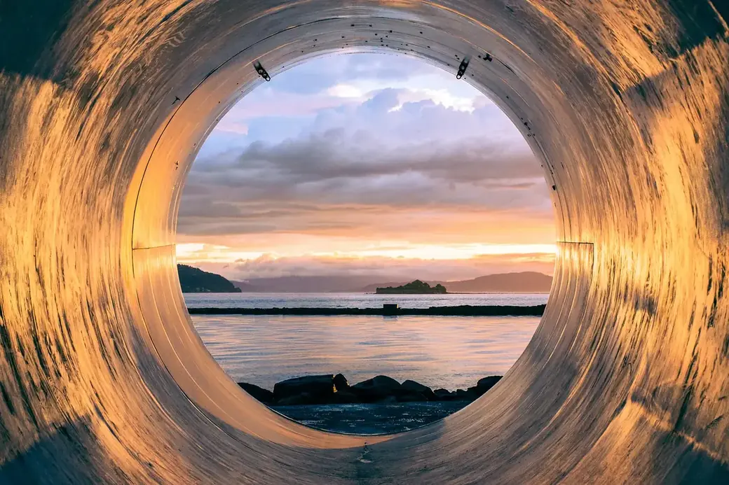 View through a large pipe onto the sea at sunset
